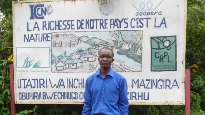 Méschac Nakanywenge, standing in front of a large poster reading "La richesse de notre pays c'est la nature".