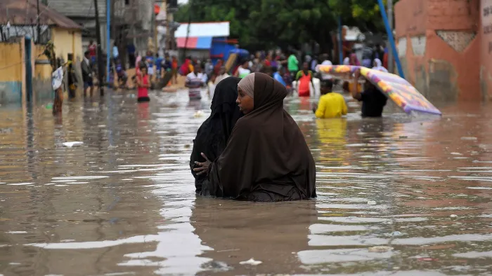 Two women walk together in floodwater in Somalia as other people are seen carrying their belongings away from the water.