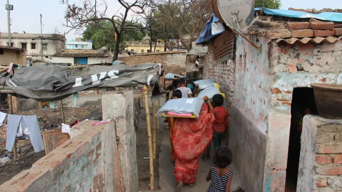 women walk into a narrow village street holding NFI kits over their heads