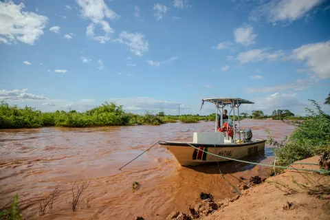 A boat is seen anchored on a drying river-bed with red mud. A man is working on the boat.