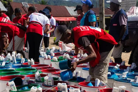 A man in a red Medair vest bends down to set up non-food items during the emergency response in Madagascar.