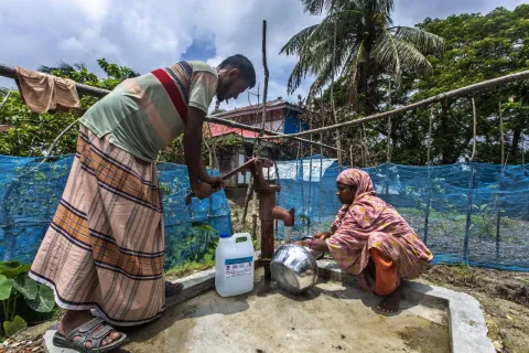 A man and a woman use a hand pump to fill clean water in cans.