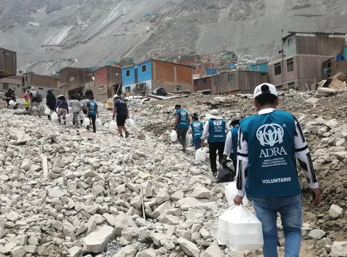 People walk through rubble in the aftermath of landsliding in Peru, to deliver hot meals to affected communities.