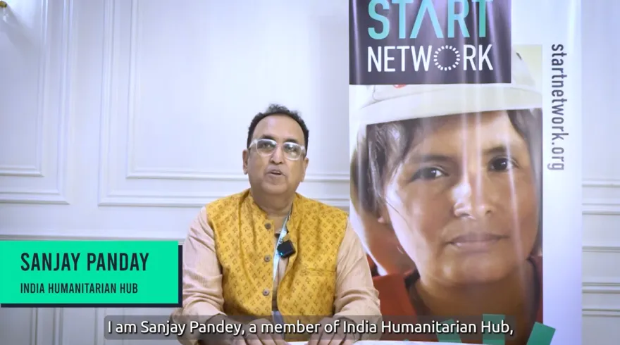 A man is sitting in front of banners with Start Network branding, as he gives an interview.