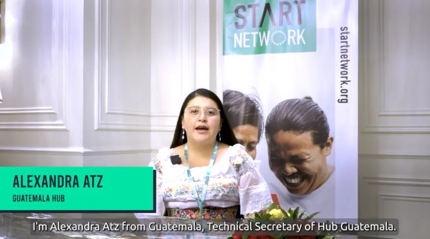 A woman speaks to the camera with Start Network banners in the background.