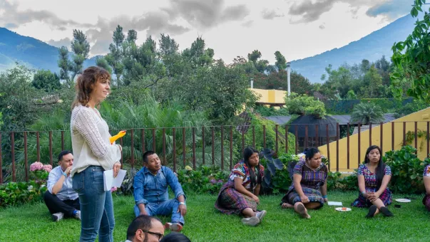 A group of people sit and stand outdoors during a session at a training in Guatemala.